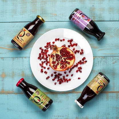 Verschiedene Flaschen Granatapfelsaft auf dem Tisch und Granatapfelkerne auf einem Teller