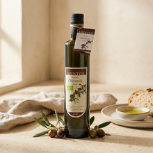 Flasche ARISTOS Natives Olivenöl Extra 500 ml auf einem Tisch, daneben Brot und ein Schälchen mit Olivenöl